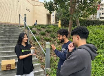 Ambassador handing a product to students on campus steps